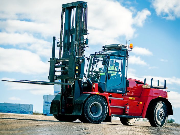 Outdoor shot of a large dark gray/black forklift with a red body and extending lift arm.